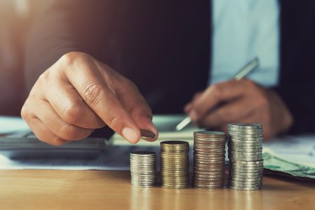 concept saving money. hand holding coins putting stack on table in office